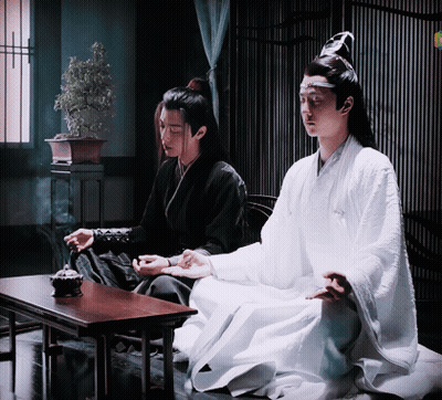 Two Men Are Sitting At A Table In A Room . One Of The Men Is Wearing A White Robe . GIF