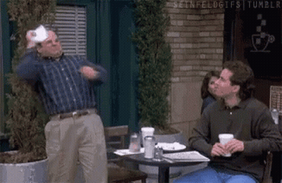 Two Men Are Sitting At A Table In Front Of A Brick Building . GIF