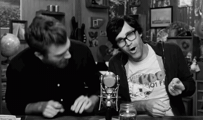 Two Men Are Sitting At A Table In Front Of A Microphone Talking To Each Other . GIF