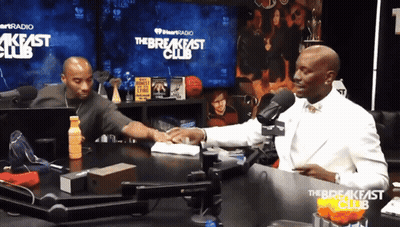 Two Men Are Sitting At A Table In Front Of A Sign That Says The Breakfast Club GIF