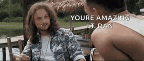 Two Men Are Sitting At A Table Talking To Each Other . One Of The Men Is Wearing A Hawaiian Shirt . GIF