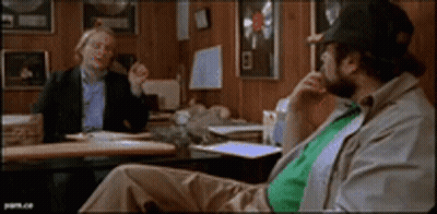Two Men Are Sitting At A Table Talking To Each Other GIF