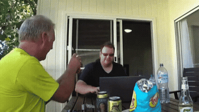 Two Men Are Sitting At A Table With A Bag Of Chips And A Can Of Schweppes On It GIF