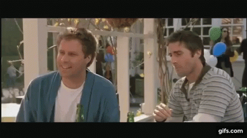 Two Men Are Sitting At A Table With A Bottle Of Beer And Smiling . GIF