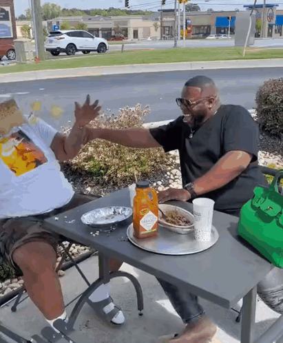 Two Men Are Sitting At A Table With A Bottle Of Tabasco Ketchup On It GIF