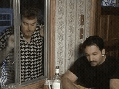 Two Men Are Sitting At A Table With A Bottle Of Vodka In Front Of Them And One Of Them Is Smoking A Cigarette . GIF