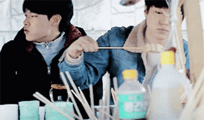 Two Men Are Sitting At A Table With A Bottle That Says 820 GIF