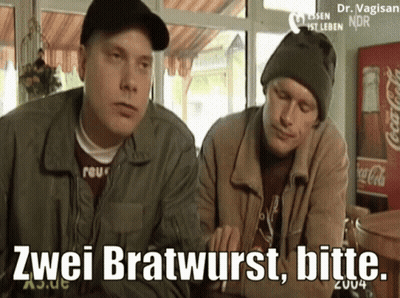 Two Men Are Sitting At A Table With A Coca Cola Fridge In The Background GIF