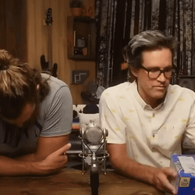 Two Men Are Sitting At A Table With A Microphone And A Box Of Cheerios GIF
