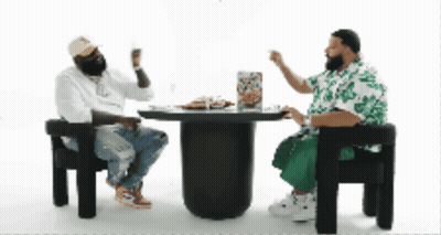 Two Men Are Sitting At A Table With A Pizza On It GIF