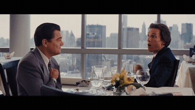 Two Men Are Sitting At A Table With A View Of The City In The Background GIF
