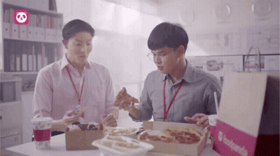 Two Men Are Sitting At A Table With Boxes Of Food And A Bag That Says Foodpanda On It GIF