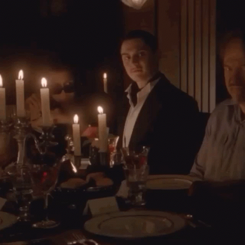 Two Men Are Sitting At A Table With Candles Lit GIF