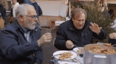 Two Men Are Sitting At A Table With Plates Of Food GIF