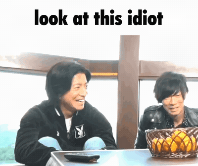 Two Men Are Sitting At A Table With The Words Look At This Idiot Written Above Them GIF