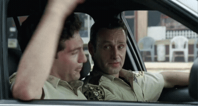 Two Men Are Sitting In A Car And One Has A Sheriff 'S Badge On His Shirt GIF