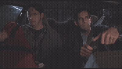 Two Men Are Sitting In A Car And One Of Them Is Holding A Red Bag GIF