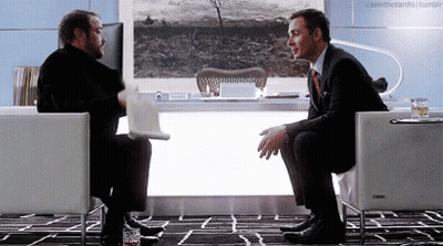 Two Men Are Sitting In Chairs Talking To Each Other GIF