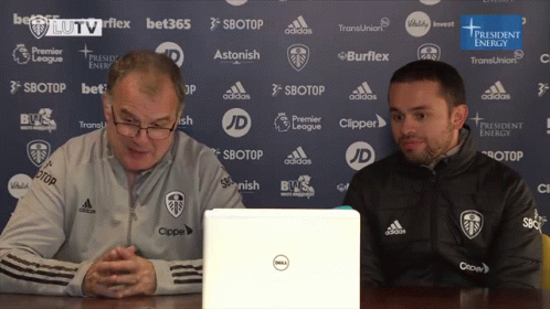 Two Men Are Sitting In Front Of A Dell Laptop In Front Of A Blue Backdrop GIF