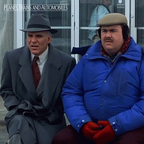 Two Men Are Sitting In Front Of A Door That Says Planes Trains And Automobiles On It GIF