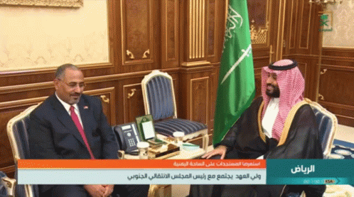 Two Men Are Sitting In Front Of A Green And White Flag And A Sign That Says Riyadh GIF
