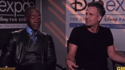 Two Men Are Sitting In Front Of A Sign That Says Disney Fan Expo GIF