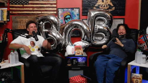Two Men Are Sitting In Front Of Balloons That Spell Out Bob GIF