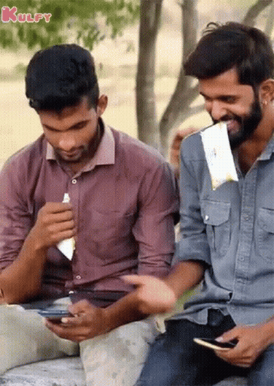 Two Men Are Sitting Next To Each Other And One Of Them Is Eating A Snack GIF