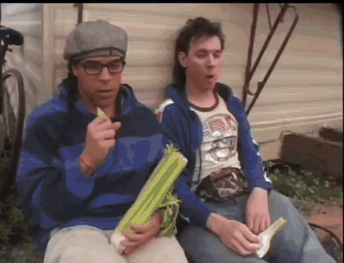 Two Men Are Sitting Next To Each Other And One Of Them Is Holding A Piece Of Celery GIF