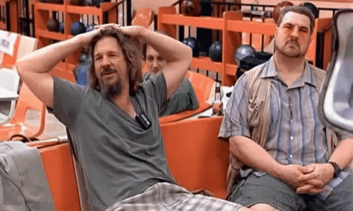 Two Men Are Sitting Next To Each Other In A Bowling Alley With Their Hands On Their Heads . GIF