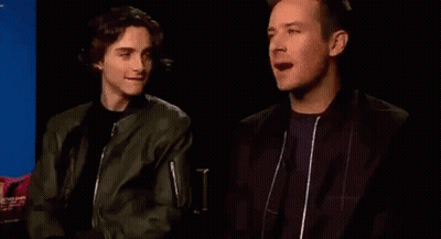 Two Men Are Sitting Next To Each Other In A Dark Room And Talking To Each Other . GIF