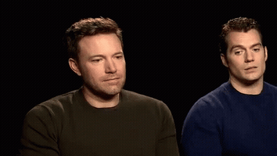Two Men Are Sitting Next To Each Other In A Dark Room And Talking To Each Other . GIF