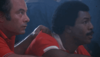 Two Men Are Sitting Next To Each Other In A Dark Room . GIF