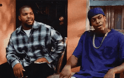 Two Men Are Sitting Next To Each Other In Front Of A Building . GIF