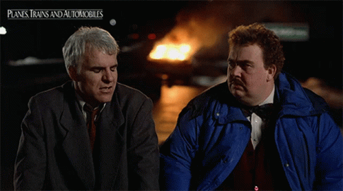 Two Men Are Sitting Next To Each Other In Front Of A Planes Trains And Automobiles Sign GIF