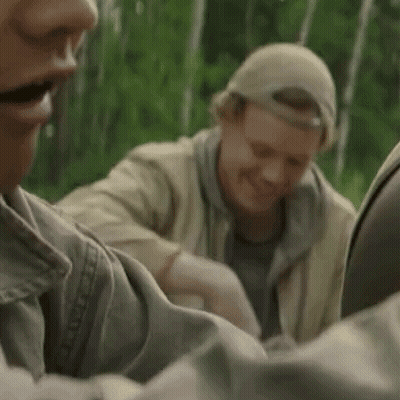 Two Men Are Sitting Next To Each Other In The Woods . GIF