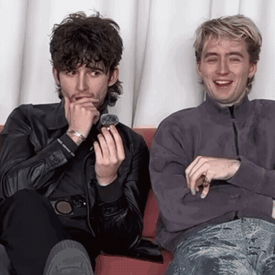 Two Men Are Sitting Next To Each Other On A Couch And One Is Holding A Ring In His Hand . GIF