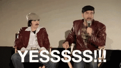 Two Men Are Sitting Next To Each Other On A Couch And One Of Them Is Holding A Microphone And Saying Yesssss ! GIF
