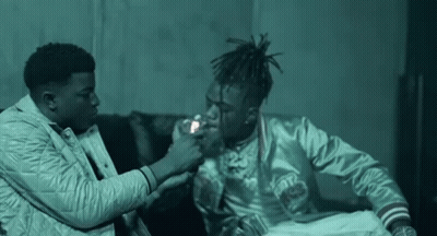 Two Men Are Sitting Next To Each Other On A Couch And One Of Them Is Lighting The Other 'S Cigarette . GIF