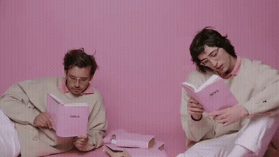 Two Men Are Sitting Next To Each Other Reading Books . GIF