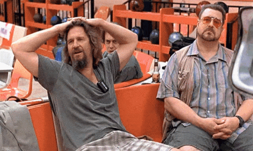 Two Men Are Sitting On A Bench In A Bowling Alley With Their Hands On Their Heads . GIF