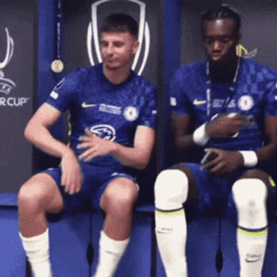 Two Men Are Sitting On A Bench In A Locker Room . GIF