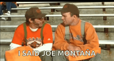 Two Men Are Sitting On A Bleacher Talking To Each Other And One Of Them Is Wearing An Orange Shirt . GIF