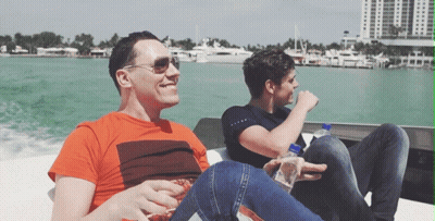 Two Men Are Sitting On A Boat In The Water And One Has A Bottle Of Aquafina Water In His Hand GIF