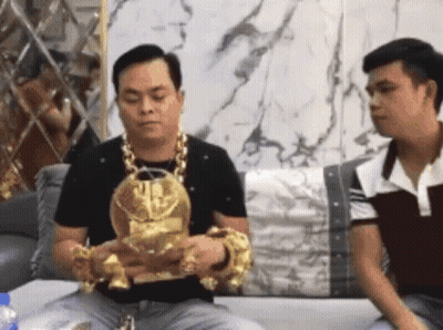 Two Men Are Sitting On A Couch And One Of Them Is Wearing A Gold Necklace And Bracelets GIF