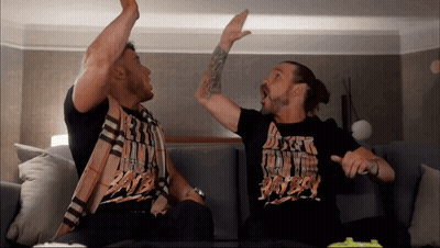 Two Men Are Sitting On A Couch And One Of Them Is Wearing A Shirt That Says ' Dirty Boy ' GIF