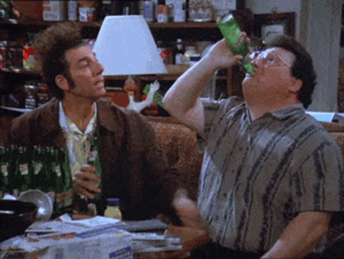 Two Men Are Sitting On A Couch Drinking Soda From Green Bottles GIF