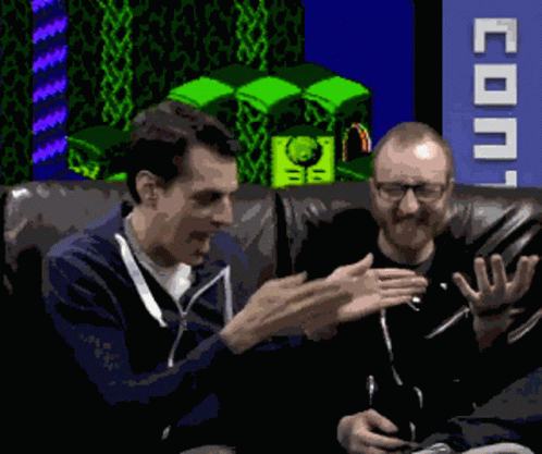 Two Men Are Sitting On A Couch In Front Of A Sign That Says Coin GIF