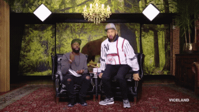 Two Men Are Sitting On A Couch In Front Of A Wall With Trees And The Word Viceland On It GIF