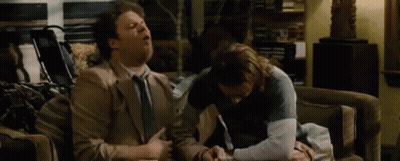 Two Men Are Sitting On A Couch Talking To Each Other . GIF